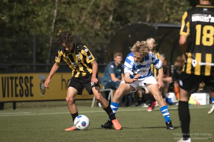 Speler van De Graafschap probeert een Vitesse-speler van de bal te zetten, nummer 18 kijkt van dichtbij toe