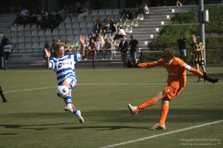 Speler van De Graafschap haalt uit terwijl de keeper in oranje zich breed maakt voor de tribune