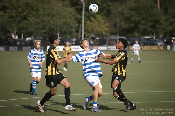 Speler van De Graafschap wacht op een hoge bal, ingeklemd tussen twee spelers van Vitesse