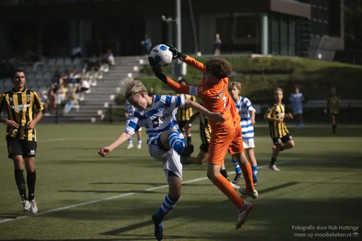 Keeper in oranje stompt de bal weg boven het hoofd van een aanvaller van De Graafschap