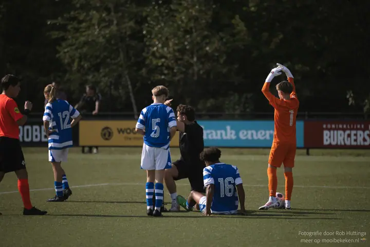 Spelers van De Graafschap staan bij teamgenoot nummer 16, die op het gras zit en wordt verzorgd