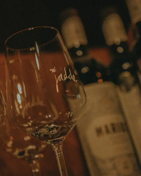 Wijnglas met het handgeschreven Jadda-logo, flessen wijn onscherp op de achtergrond