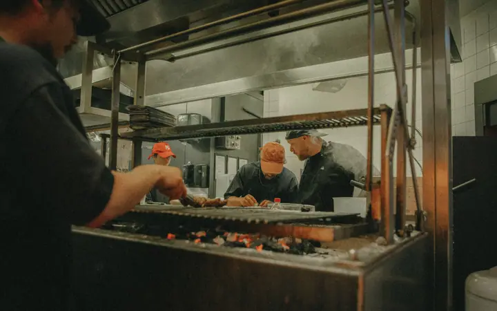 Blik over de houtskoolgrill de open keuken in, waar het team van Jadda aan het werk is