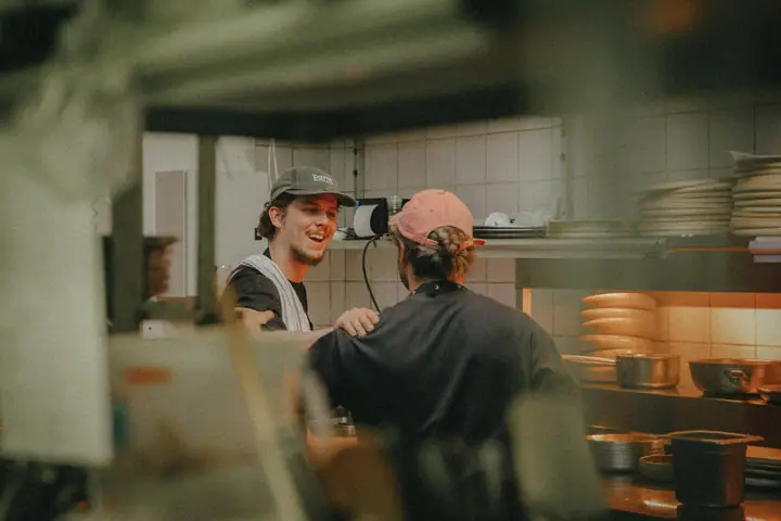 Twee koks delen een lach in de keuken, de een met een hand op de schouder van de ander