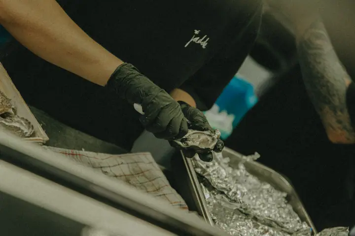 Oesters openen aan de werkbank, naast een bak met aluminiumfolie en een geruite theedoek