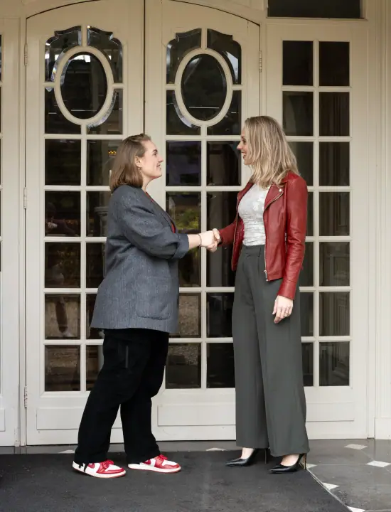 Twee vrouwen schudden elkaar de hand voor de witte deuren met ronde ramen bij de ingang