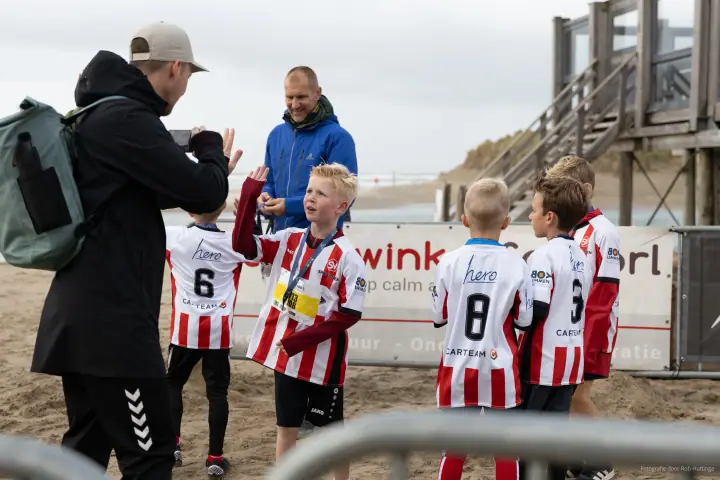 Een jonge loper geeft een high five aan een man met een telefoon, teamgenoten in gestreepte shirts erachter
