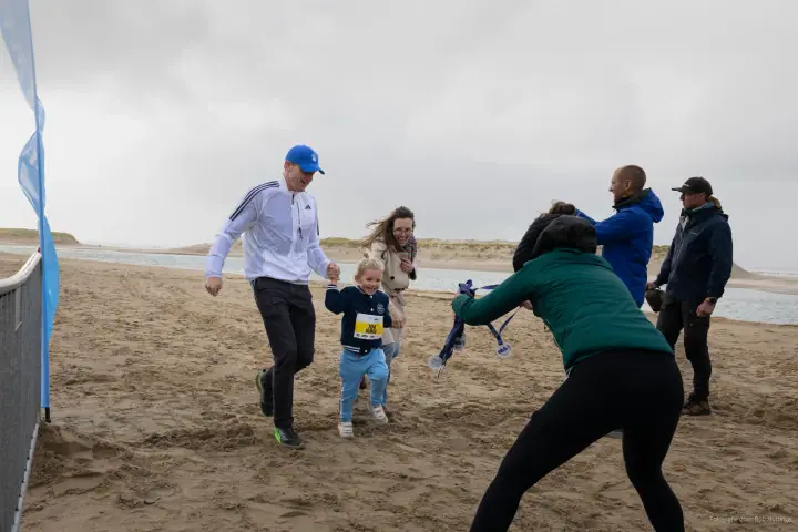 Vader rent met zijn dochtertje over het strand tijdens de kidsrun van de Mudsweattrail, met supporters erachter