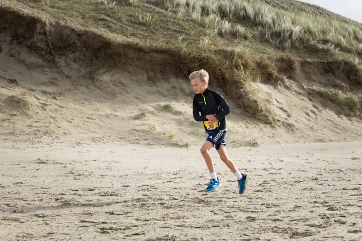 Jongen in zwart jack rent over het strand langs de voet van een steile duinrand