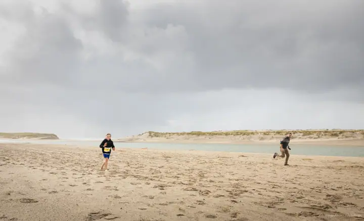 Een kind en een volwassene rennen over een leeg strand onder zware donkere wolken