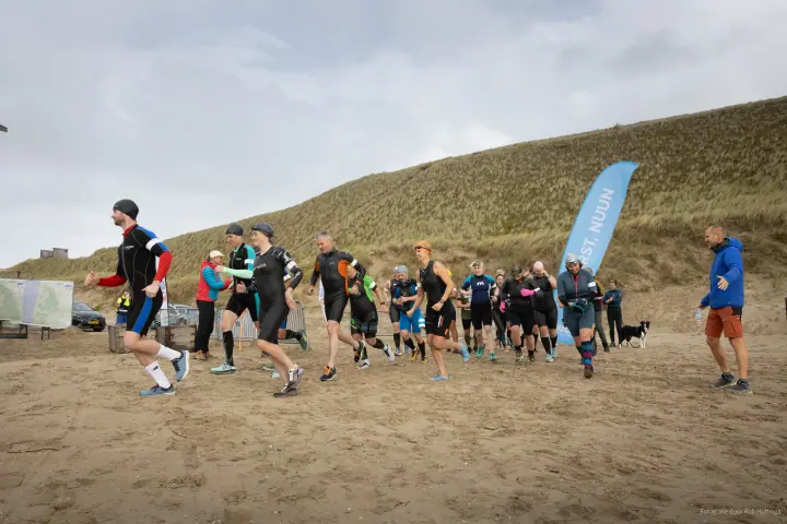 Start van MudSweatTrail op het strand, lopers in wetsuits vertrekken met de duinen achter zich