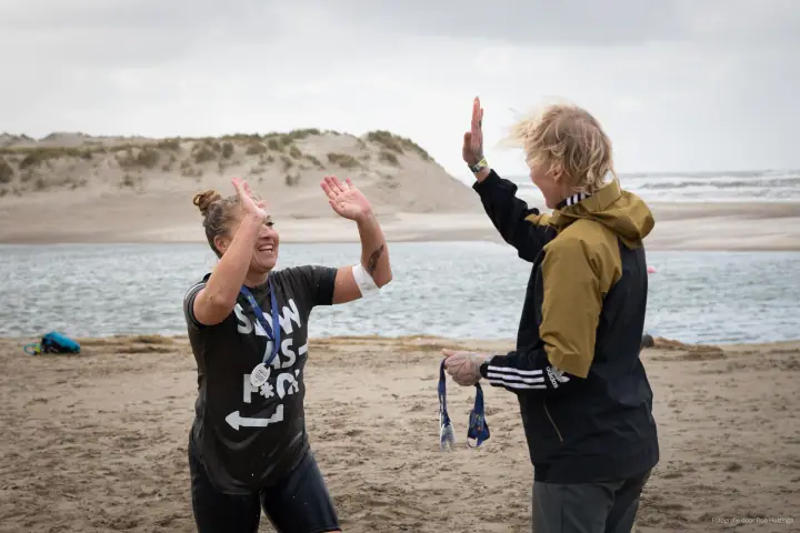 Een finisher en een vrijwilliger met medailles in haar hand geven elkaar een high five aan het water