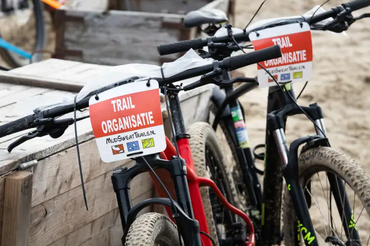 Mountainbikes met bordjes Trail Organisatie van MudSweatTrails.nl staan klaar op het strand