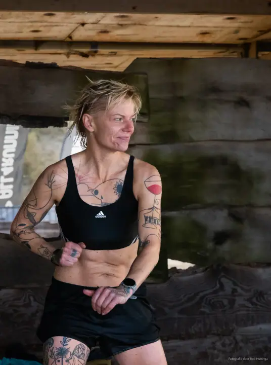 Portret van een getatoeëerde deelnemer in sporttop onder het houten paviljoen, haar haar nog nat