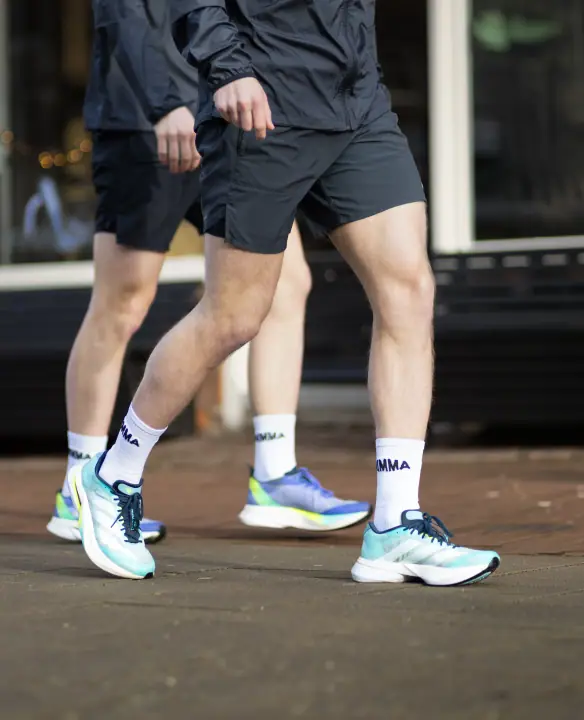 Twee hardlopers lopen over straat in witte NIMMA sokken en felgekleurde hardloopschoenen