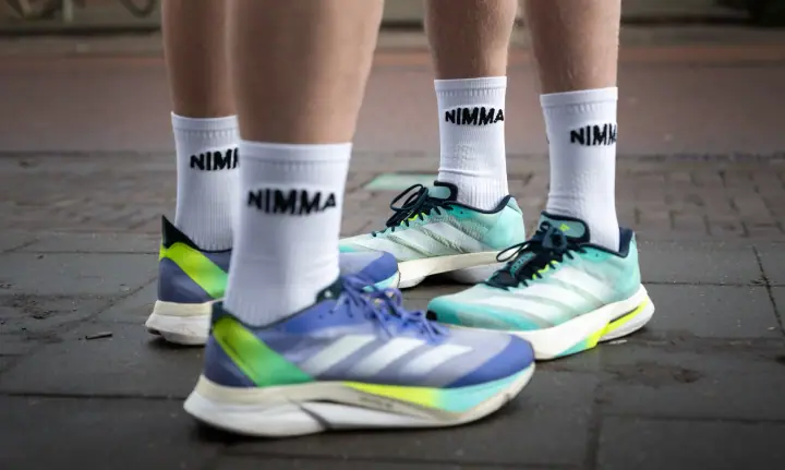 Close-up van twee paar voeten in witte NIMMA sokken en kleurrijke hardloopschoenen op de stoep