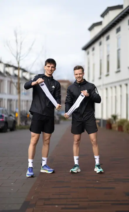 Twee lopers van Nimma Running Club laten lachend hun nieuwe sokken zien in een straat in Nijmegen