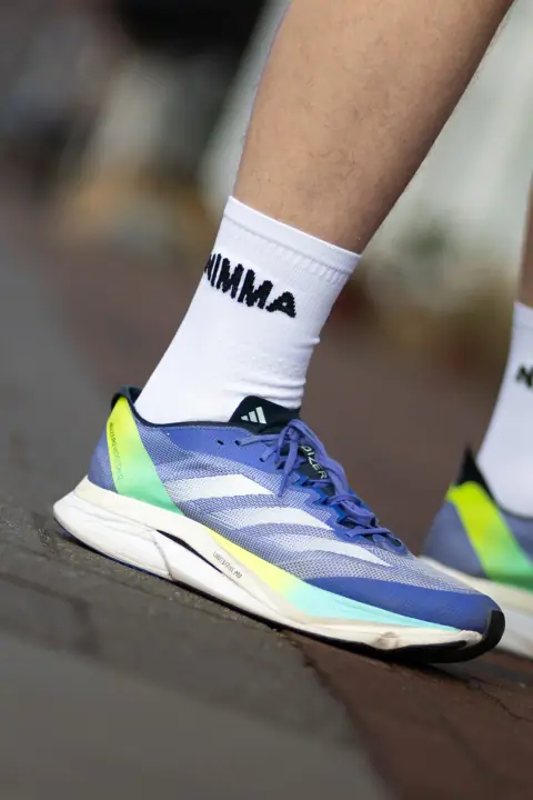 Detail van een witte NIMMA sok boven een blauwgele hardloopschoen