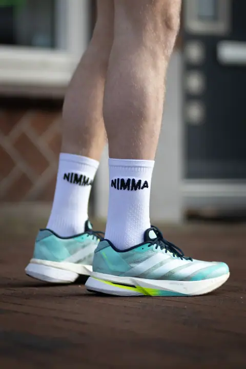Benen in witte NIMMA sokken en mintgroene hardloopschoenen op een bakstenen stoep