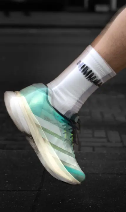 Mintgroene hardloopschoen en NIMMA sok met een dubbel belichtingseffect op donkere klinkers