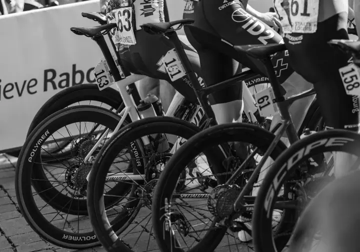 Zwart-wit detail van racefietsen met rugnummers op de zadelpennen, opgesteld achter de startlijn
