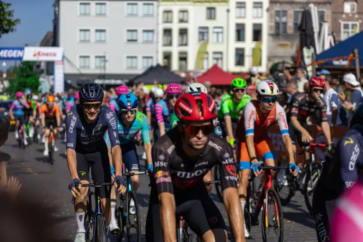 Renner met rode helm in Tudor-shirt rijdt mee in het peloton, kort na de start