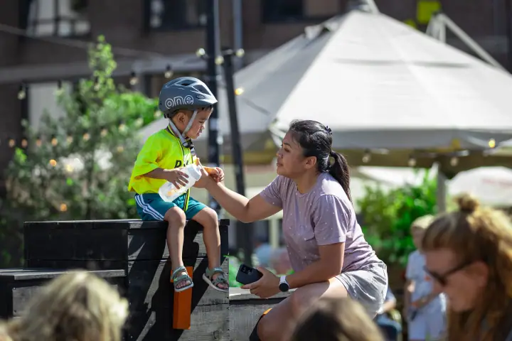 Op de rand van het podium krijgt een jonge deelnemer met fietshelm hulp bij het drinken uit een bidon