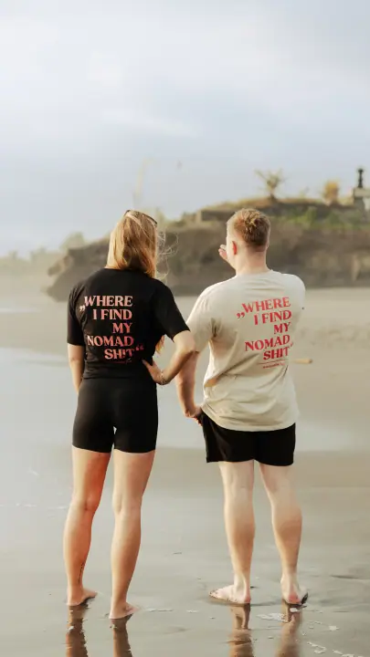 Man en vrouw staan op blote voeten aan de vloedlijn, allebei met de Nomadwise print op hun rug