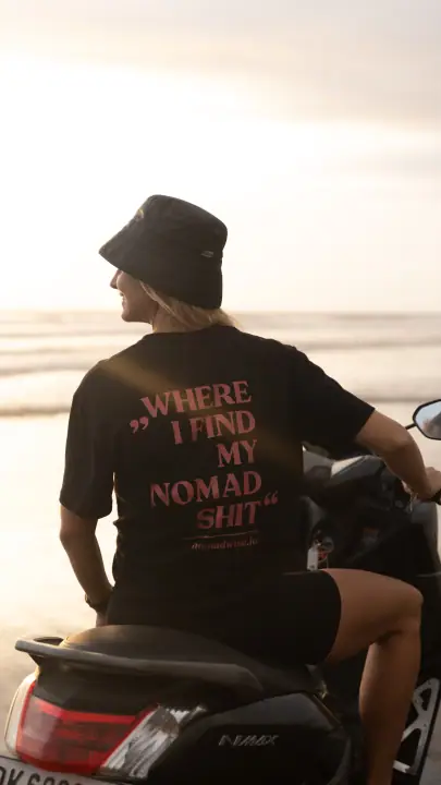 Glimlachend kijkt ze opzij vanaf de scooter, in het zwarte Nomadwise shirt en een zwart vissershoedje