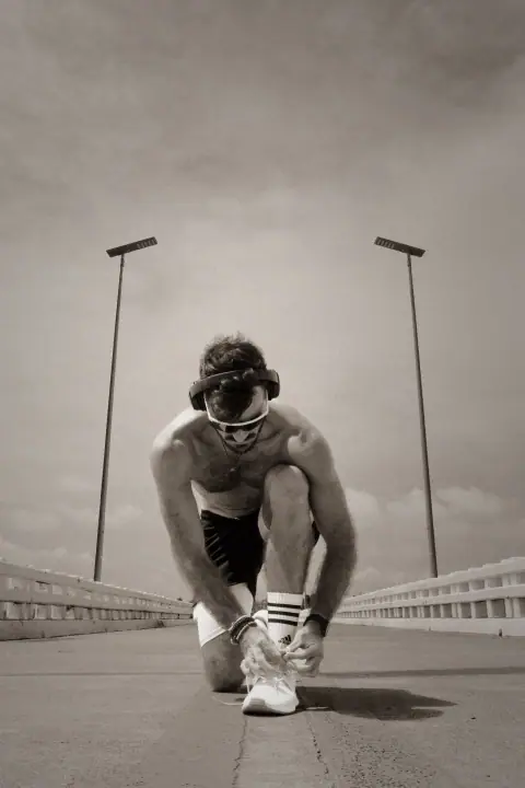 Lukas van Run Freak strikt zijn veters op een lege brug, met koptelefoon en sportbril