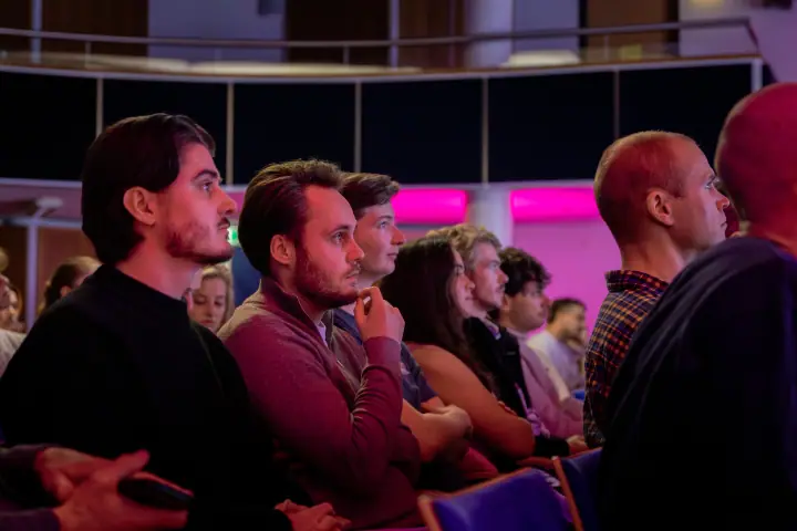Jonge mannen in het publiek luisteren geconcentreerd, eentje met zijn vuist tegen zijn kin