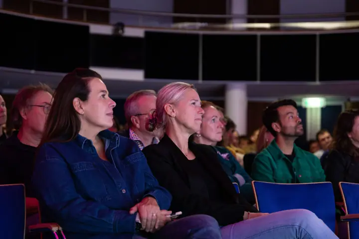 Twee vrouwen op blauwe stoelen volgen aandachtig een talk tijdens de F*ckup Night in Nijmegen