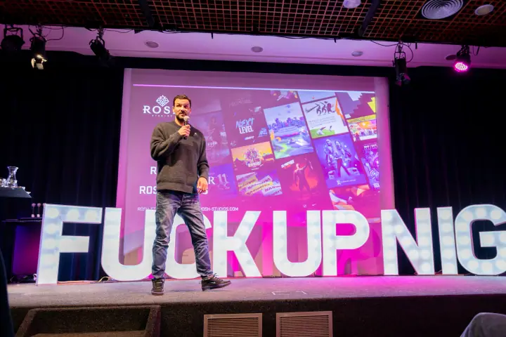 Spreker met microfoon in grijze trui en jeans, achter hem een slide vol game-artwork