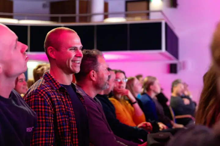 Man in geruit overhemd schiet hardop in de lach tijdens een verhaal op het podium