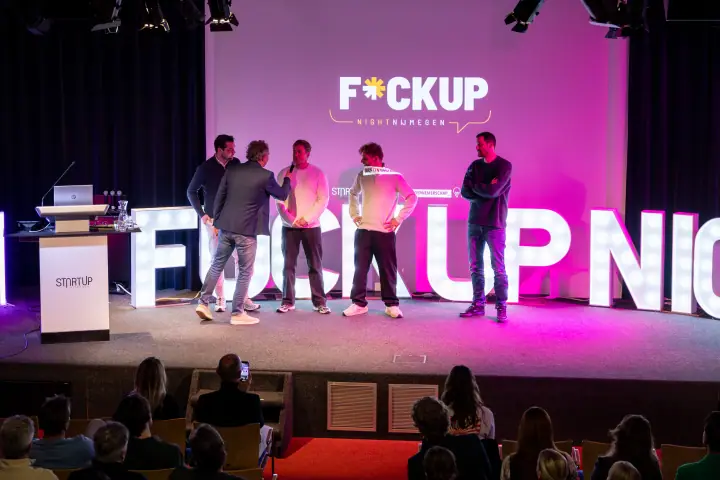 Presentator en vier sprekers samen op het podium onder het F*ckup Night logo