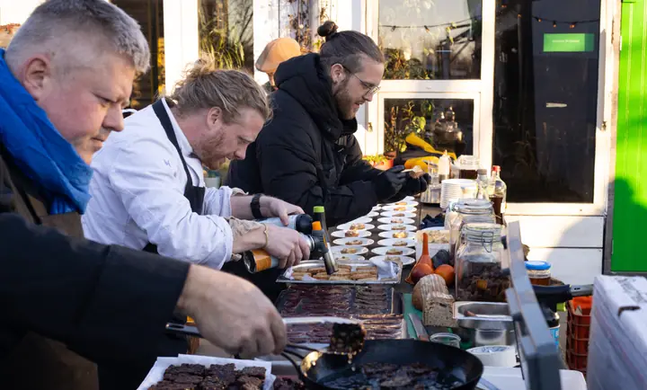 Koks aan het werk voor Uitgepolderd, met een brander, een pan en bakplaten vol hapjes