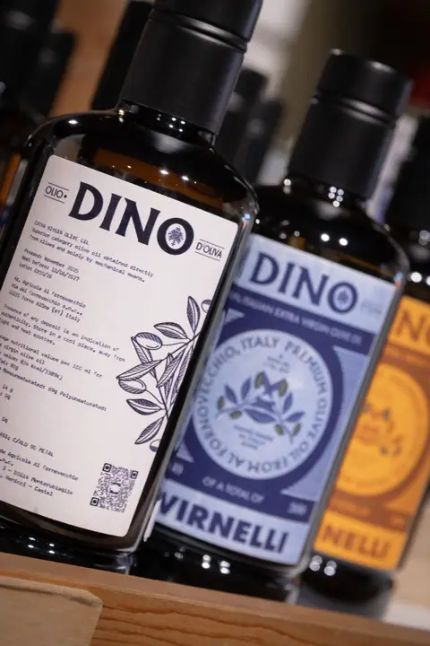Flessen DINO olijfolie in wit, blauw en oranje op een houten schap
