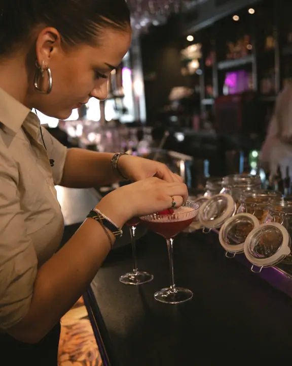 Bartender met grote oorringen werkt een rode cocktail af naast een rij weckpotten