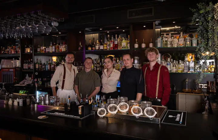 Het team van YUCA Cocktailbar met z'n vijven achter de bar, voor de volle flessenwand