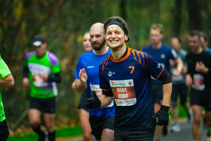 Loper met zwarte hoofdband en een blauw shirt met oranje strepen steekt grijnzend zijn duim op