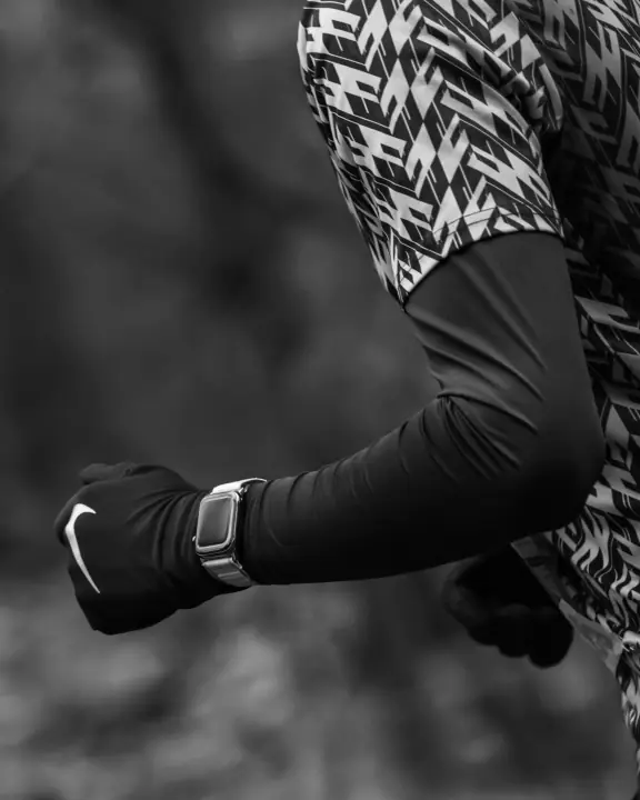 Zwart-wit detail van een gebalde vuist met Nike-handschoen en sporthorloge tijdens het lopen